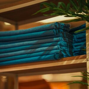 Neatly folded stack of blue towels on a wooden shelf with soft lighting.